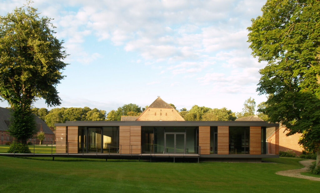 Gesamtaußenansicht des Seminargebäudes Gut Siggen mit Rasen im Vordergrund und Bäumen rechts und links