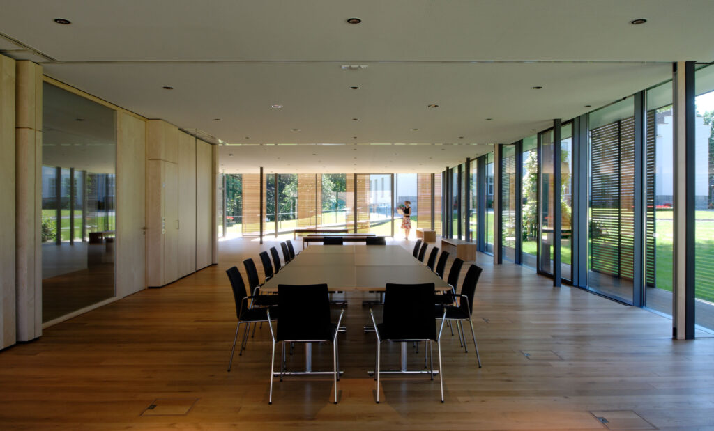 Innenansicht eines Besprechungsraumes mit Glasfront und Blick nach außen, Im hintergrund eine Frau mit Aktenordner