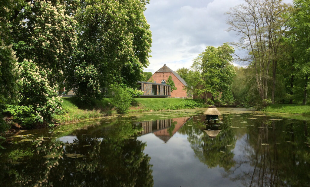 Blick über Teich auf Seminargebäude Gut Siggen mit altem Scheunengebäude im Hintergrund
