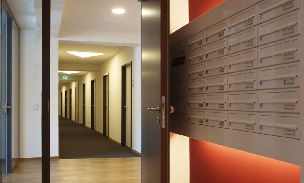 hinterleuchtete Briefkastenanlage an einer roten Wand - daneben Tür zu einem Flur mit vielen Türen