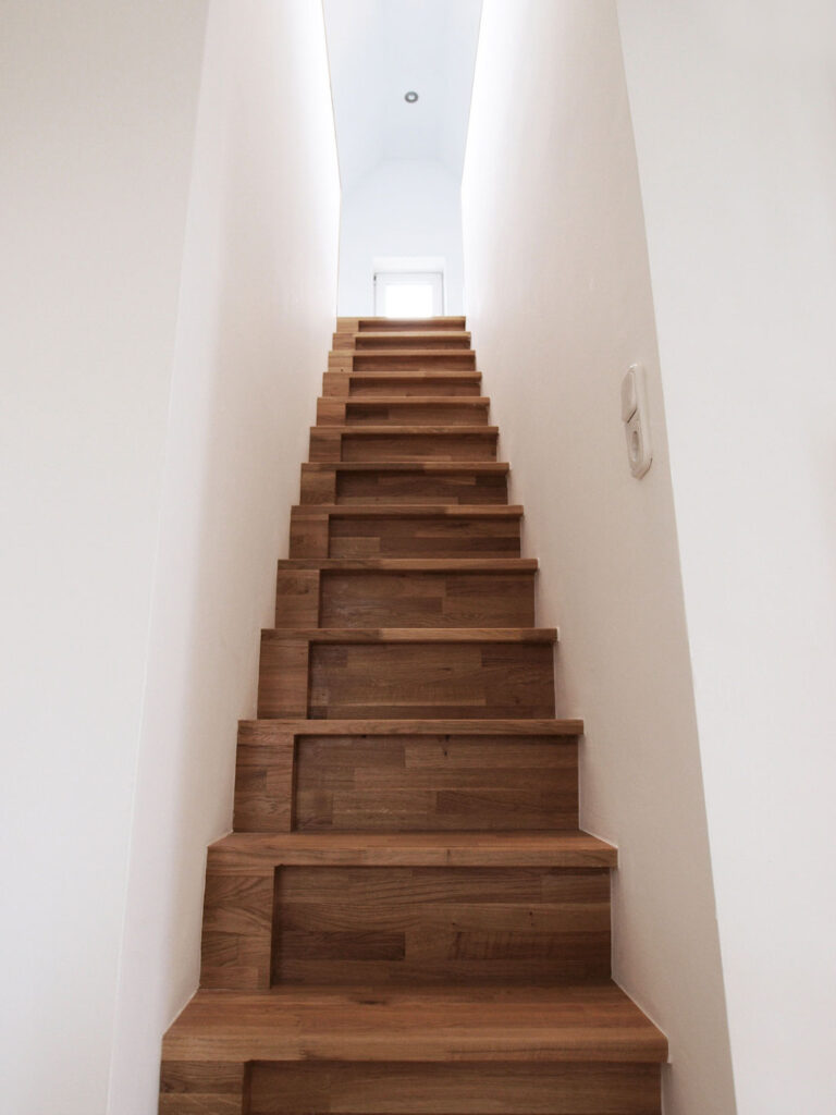 Holztreppe aufwärts zwischen weißen Wänden