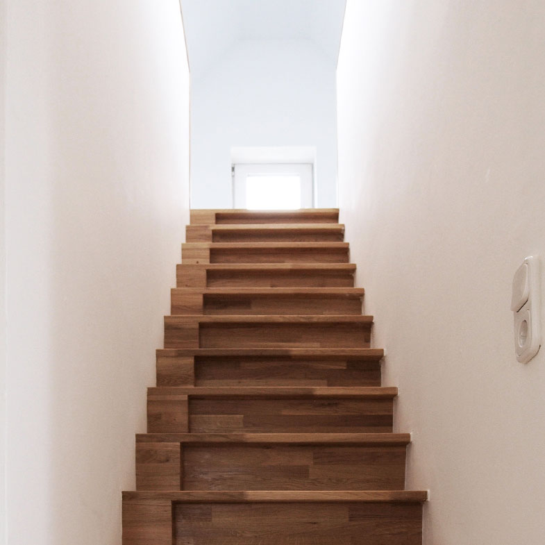 Holztreppe aufwärts zwischen weißen Wänden