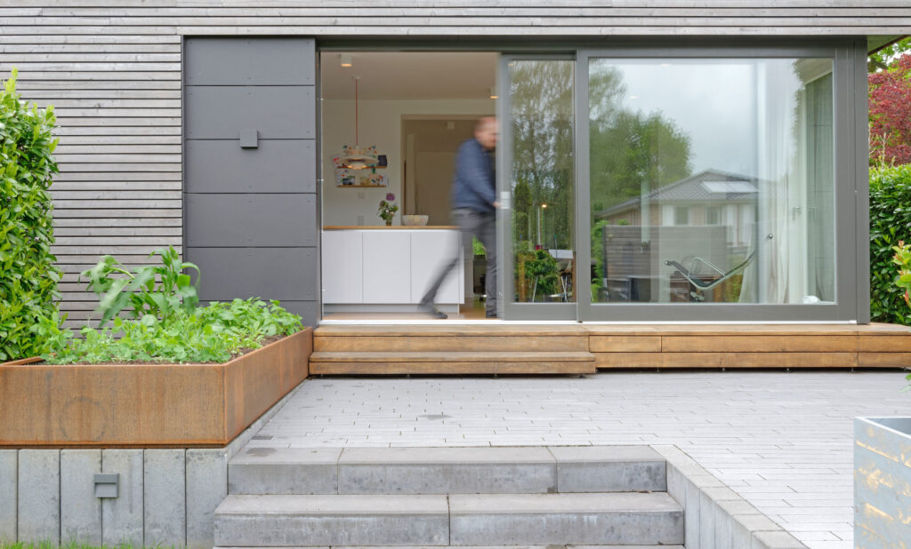 Blick von außen über Terrasse. Ein Mann öffnet eine Schiebetür