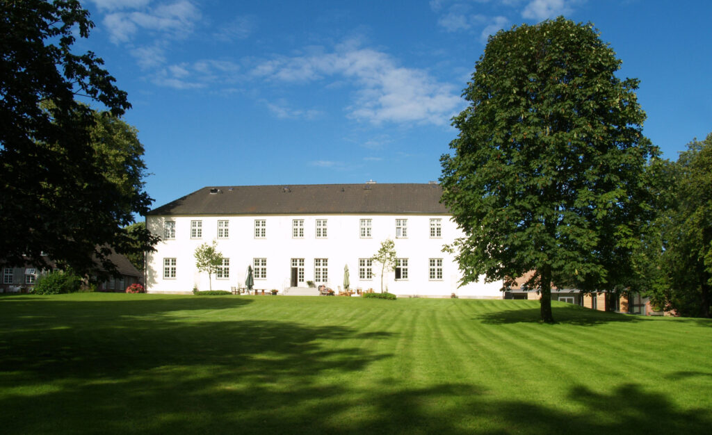 Außenansicht weißes Herrenhaus Gut Siggen mit Rasen und Bäumen im Vordergrund