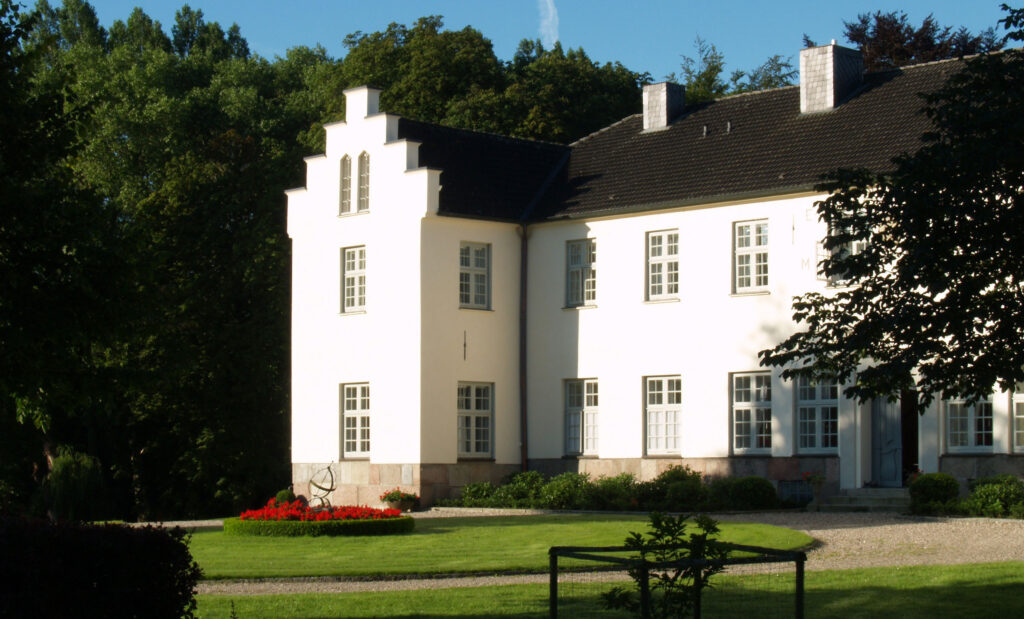 Außenansicht weißes Herrenhaus Gut Siggen, davor Rasen und Kiesweg