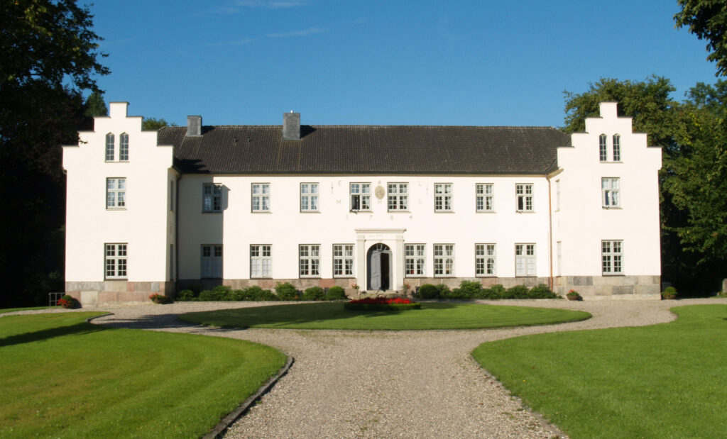 Außenansicht weißes Herrenhaus Gut Siggen, Davor Rasen und Kiesweg
