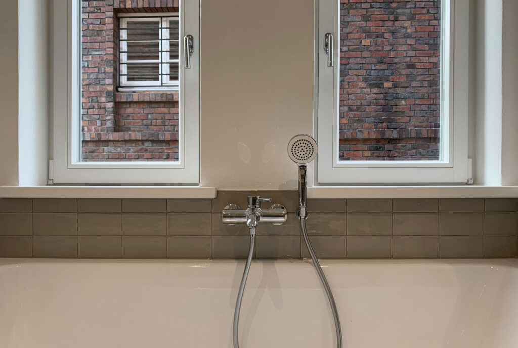 Blick auf eine Badewanne mit Duschkopf und zwei Fenster darüber