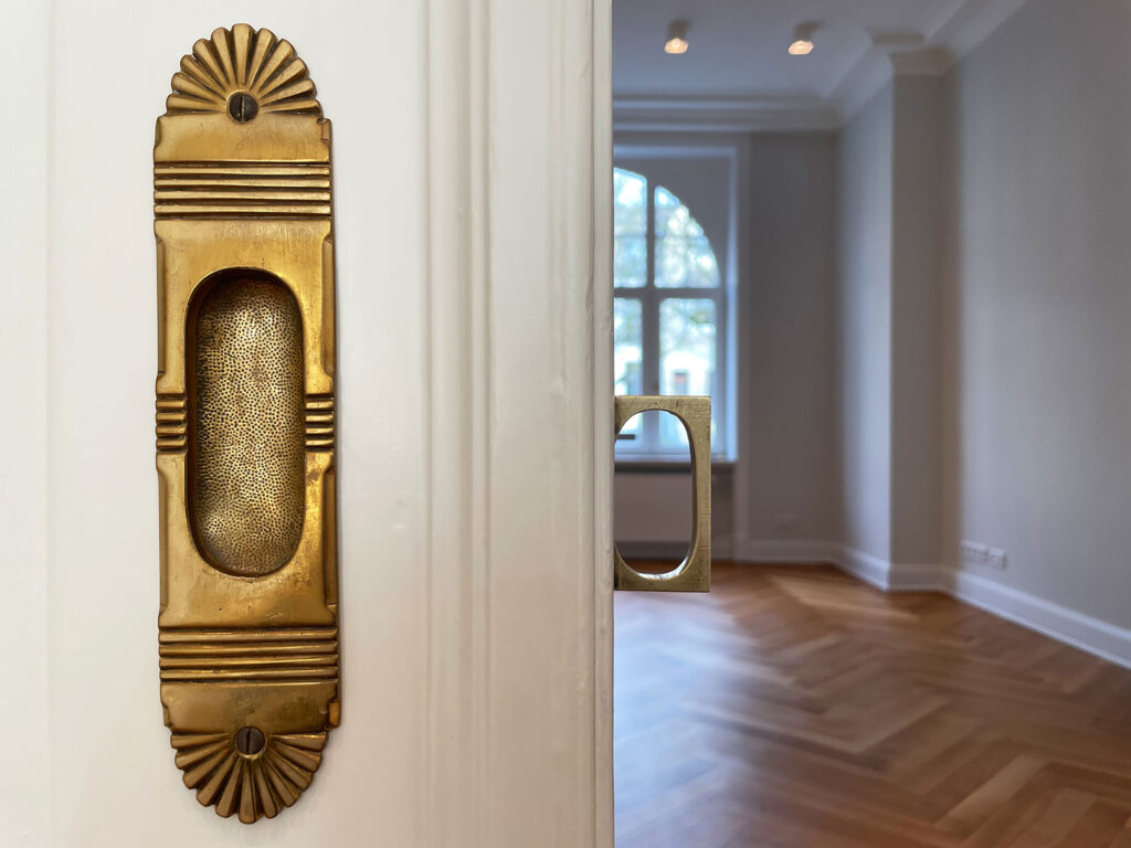 Blick in einen leeren Raum mit restauriertem Parkett - im Vordergrund eine halb geöffnete Schiebetür